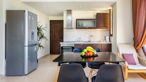 A modern kitchen with a refrigerator, microwave, and stove. There is a dining table with chairs and a fruit bowl. - Belohorizonte Fine Accommodation (Kassandra)