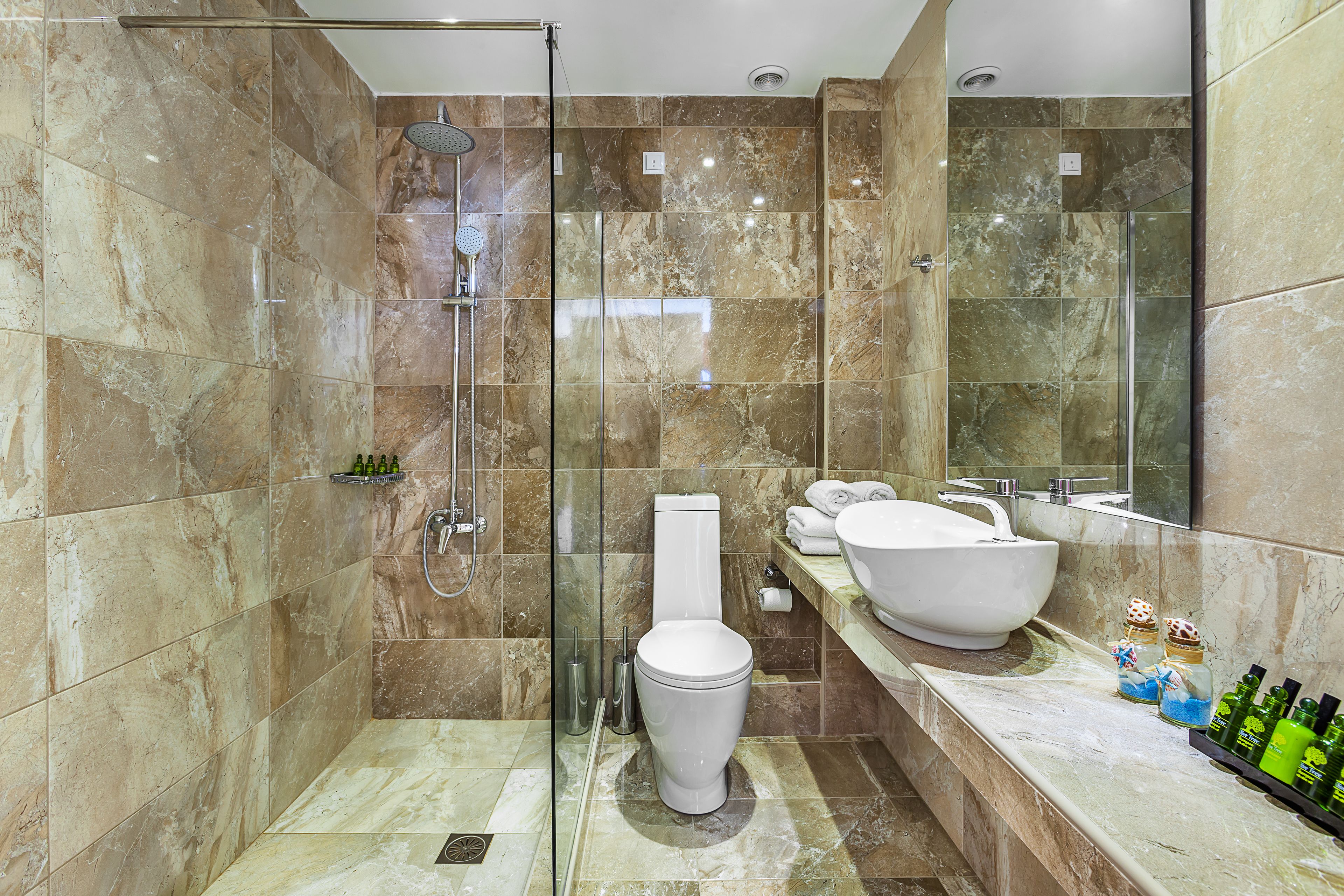 Un baño moderno con ducha envuelta en vidrio, inodoro, lavabo grande y tocador con artículos de aseo.