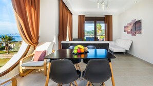 A modern dining area with a table set for two, a fruit bowl, and a view of the sea. - Belohorizonte Fine Accommodation (Kassandra)