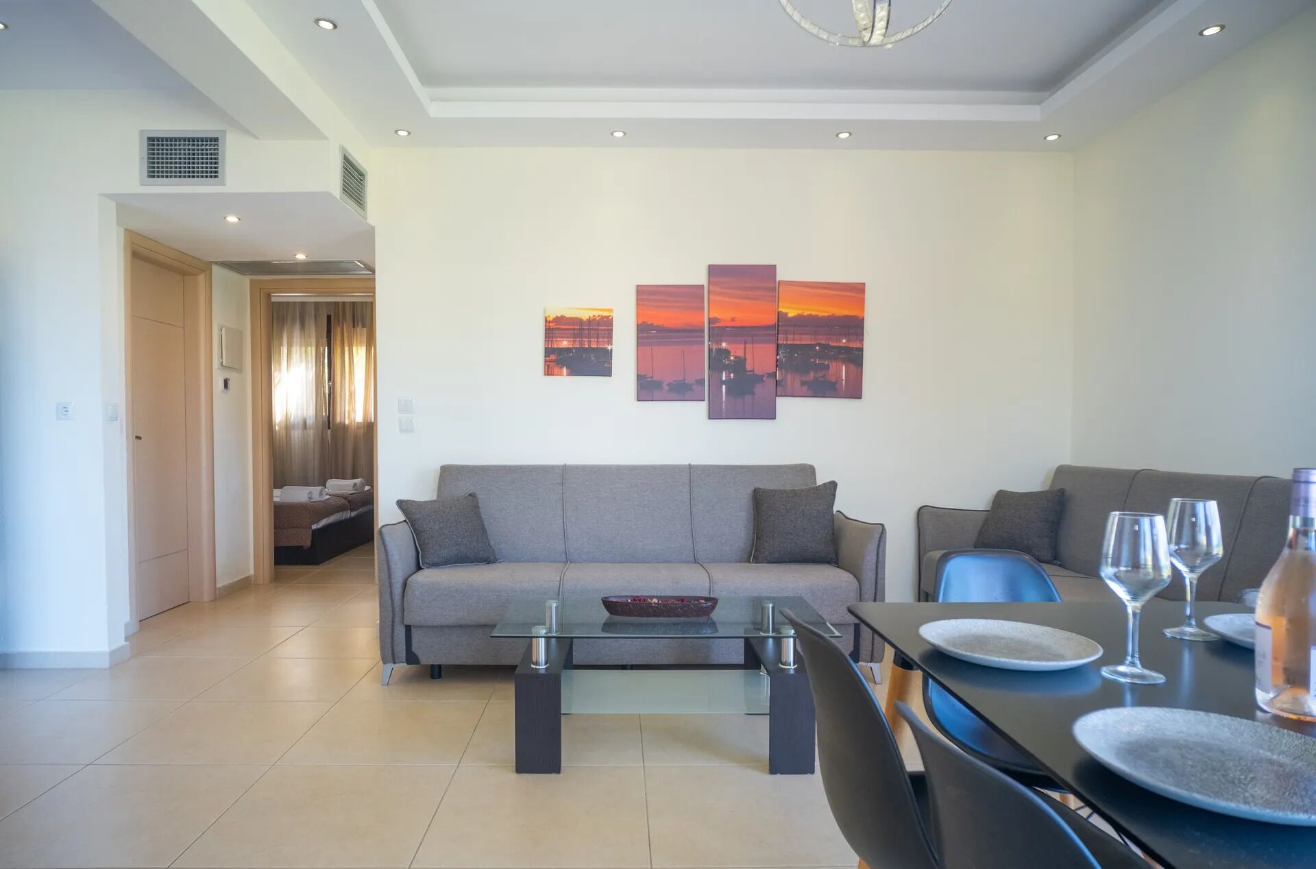 A modern living room with a sofa, a glass coffee table, and a dining area with a table set for two.
