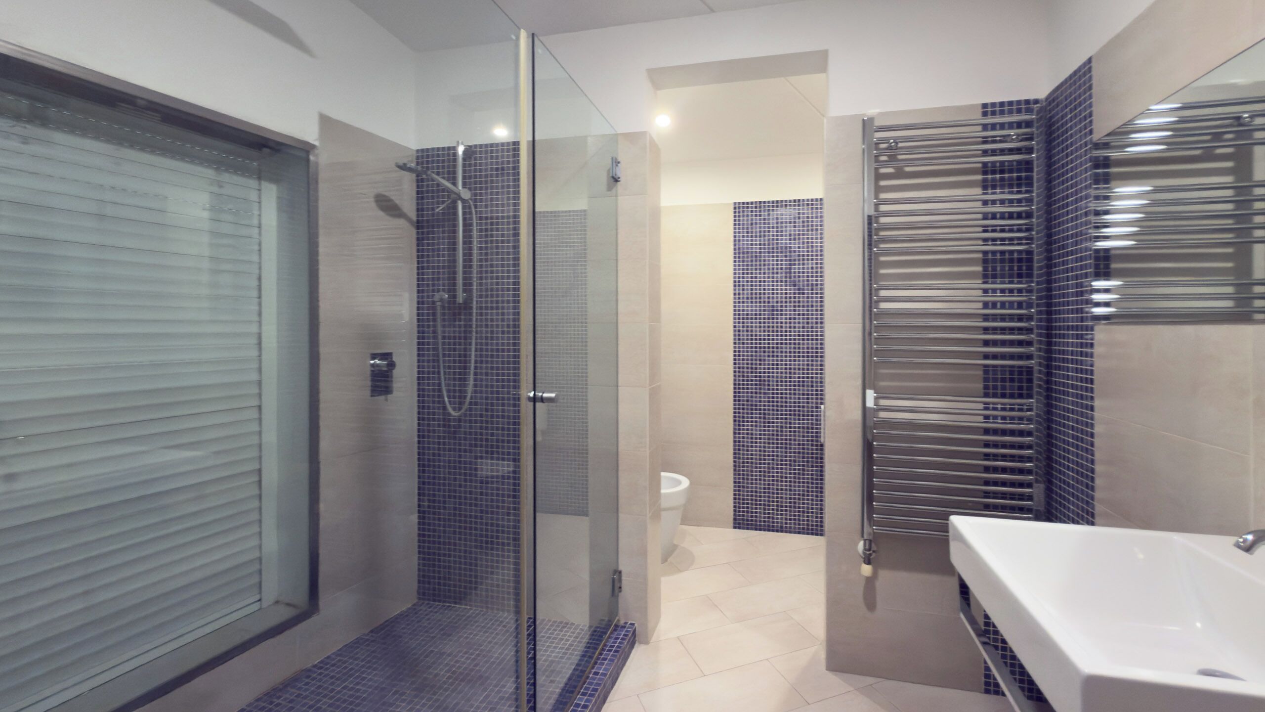 A modern bathroom with a glass-enclosed shower, a white sink, and tiled walls.
