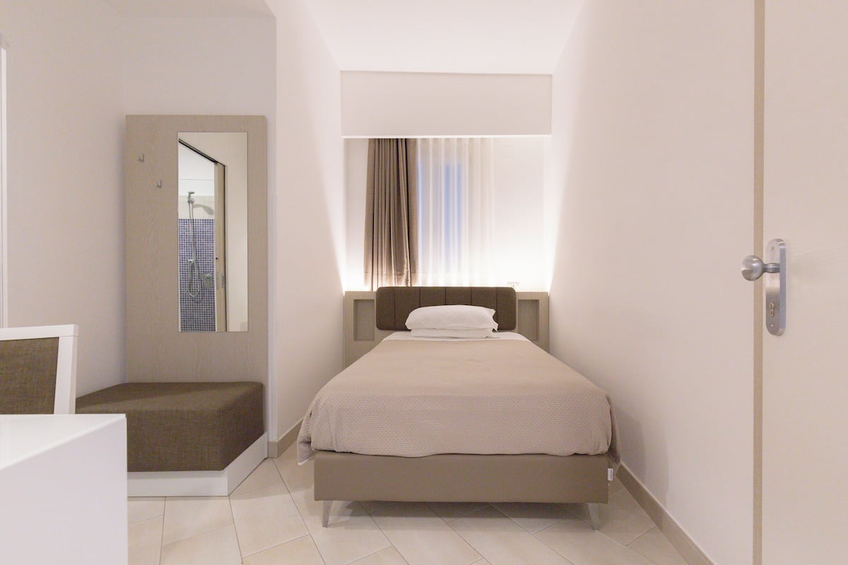 Un dormitorio con cama, mesita de noche, ventana con cortinas y puerta.