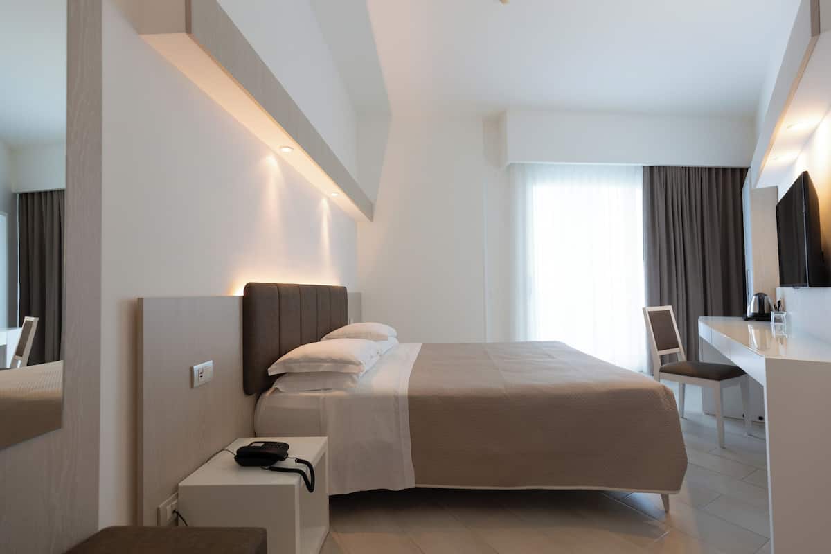 Una habitación de hotel moderna con una cama grande, un escritorio y una silla. Hay un espejo en la pared y una ventana con cortinas.
