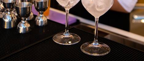 Un bar avec deux verres d’eau glacée, un barista préparant des boissons et, au fond, des étagères remplies de différentes bouteilles.