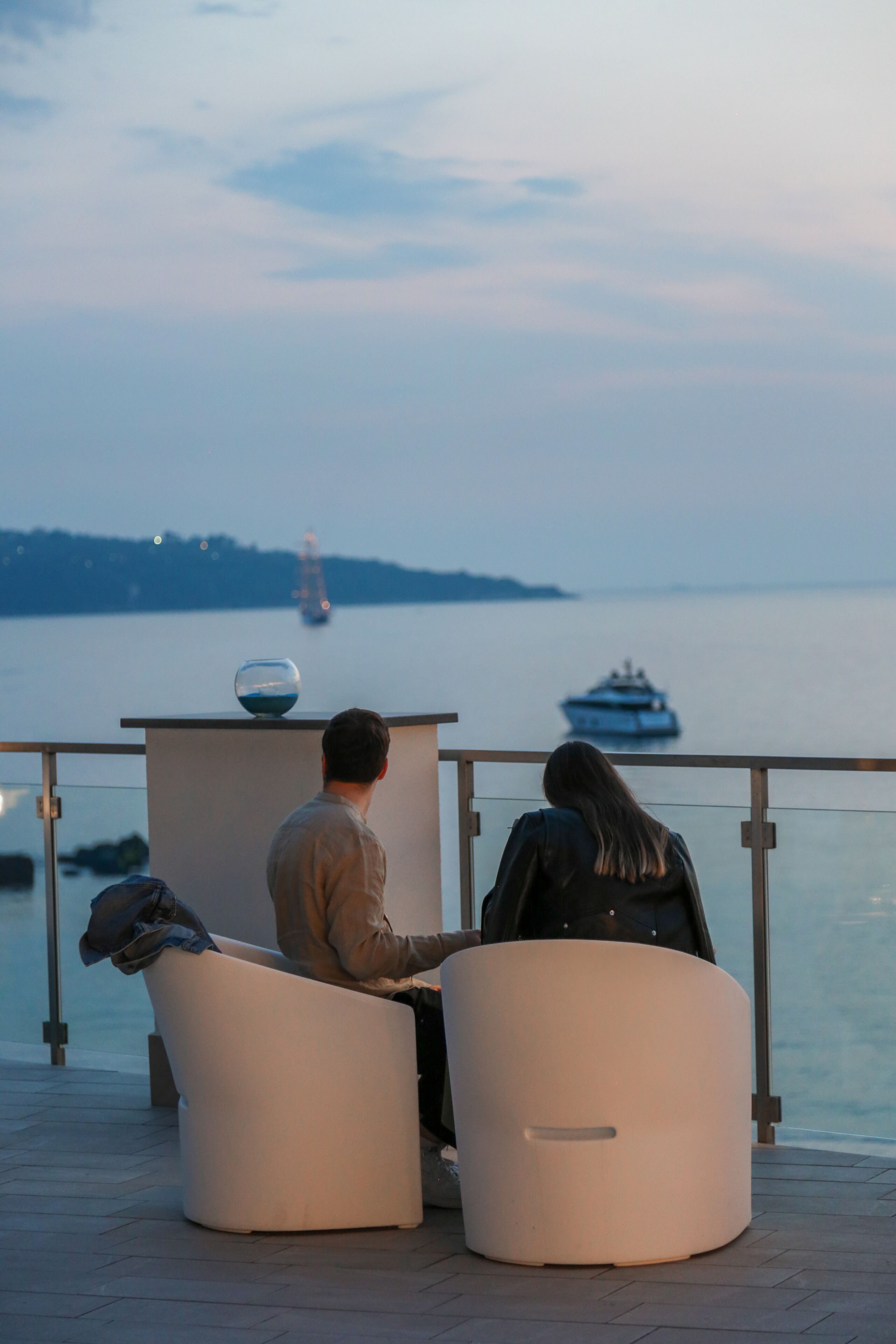 Two people seated at a table with a view of the water and a distant ship.