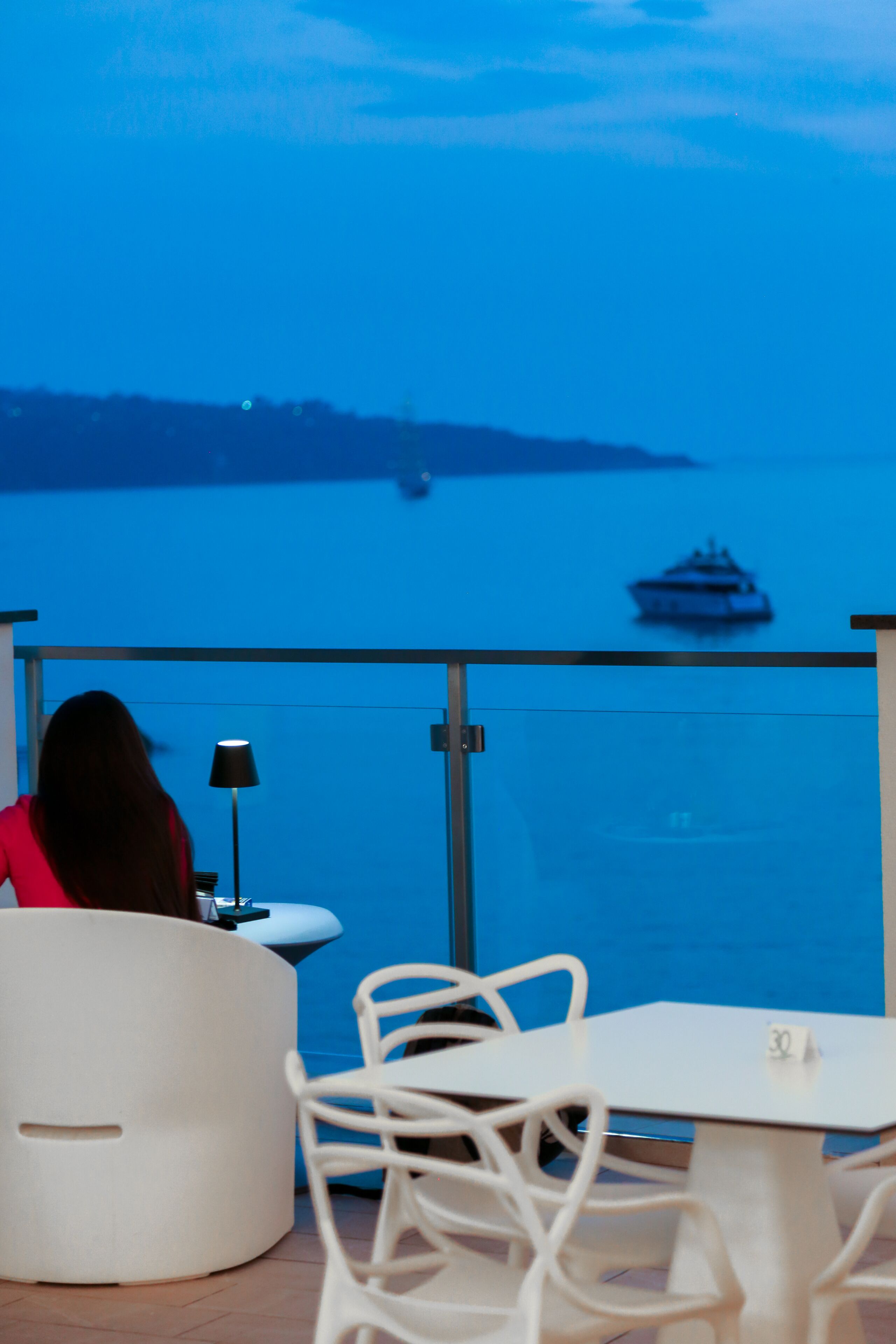 A balcony with a view of the sea, a table, and a chair.