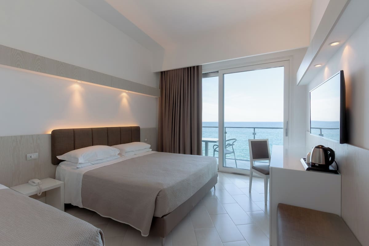 Habitación de hotel con una cama grande, un escritorio con silla, cafetera y vista al mar.