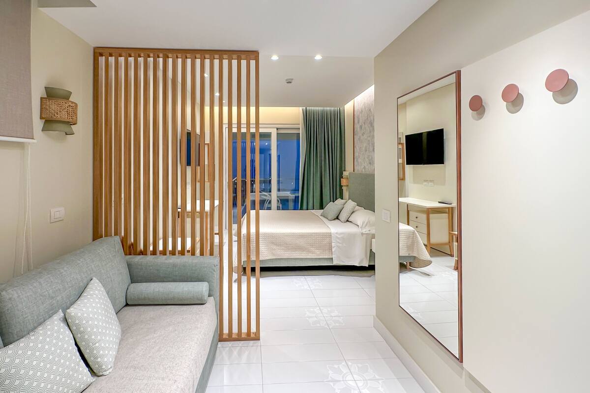 Habitación de hotel moderna con sofá, cama, espejo y vistas al exterior.