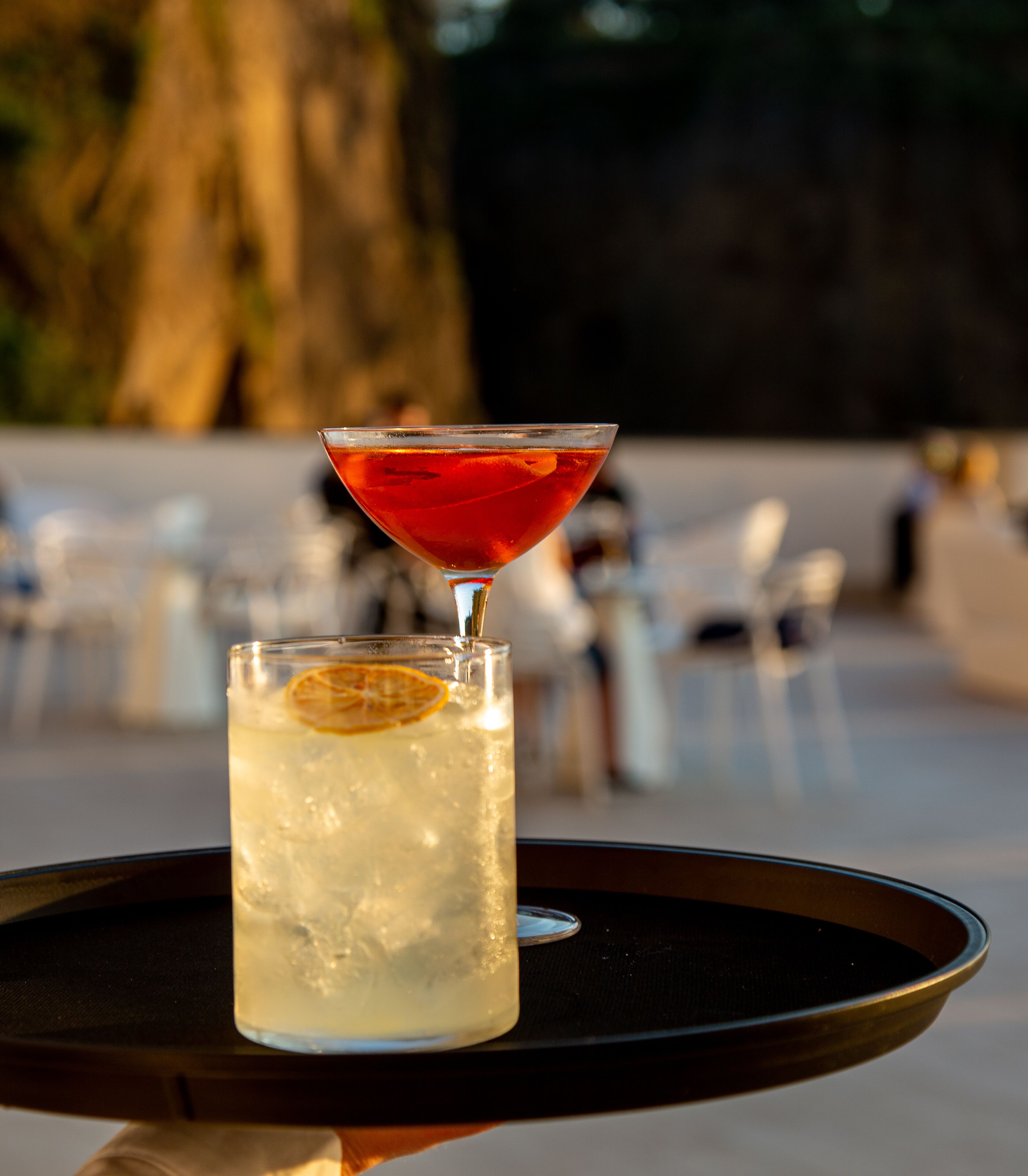 A martini glass and a tall glass with a lemon slice on a tray.
