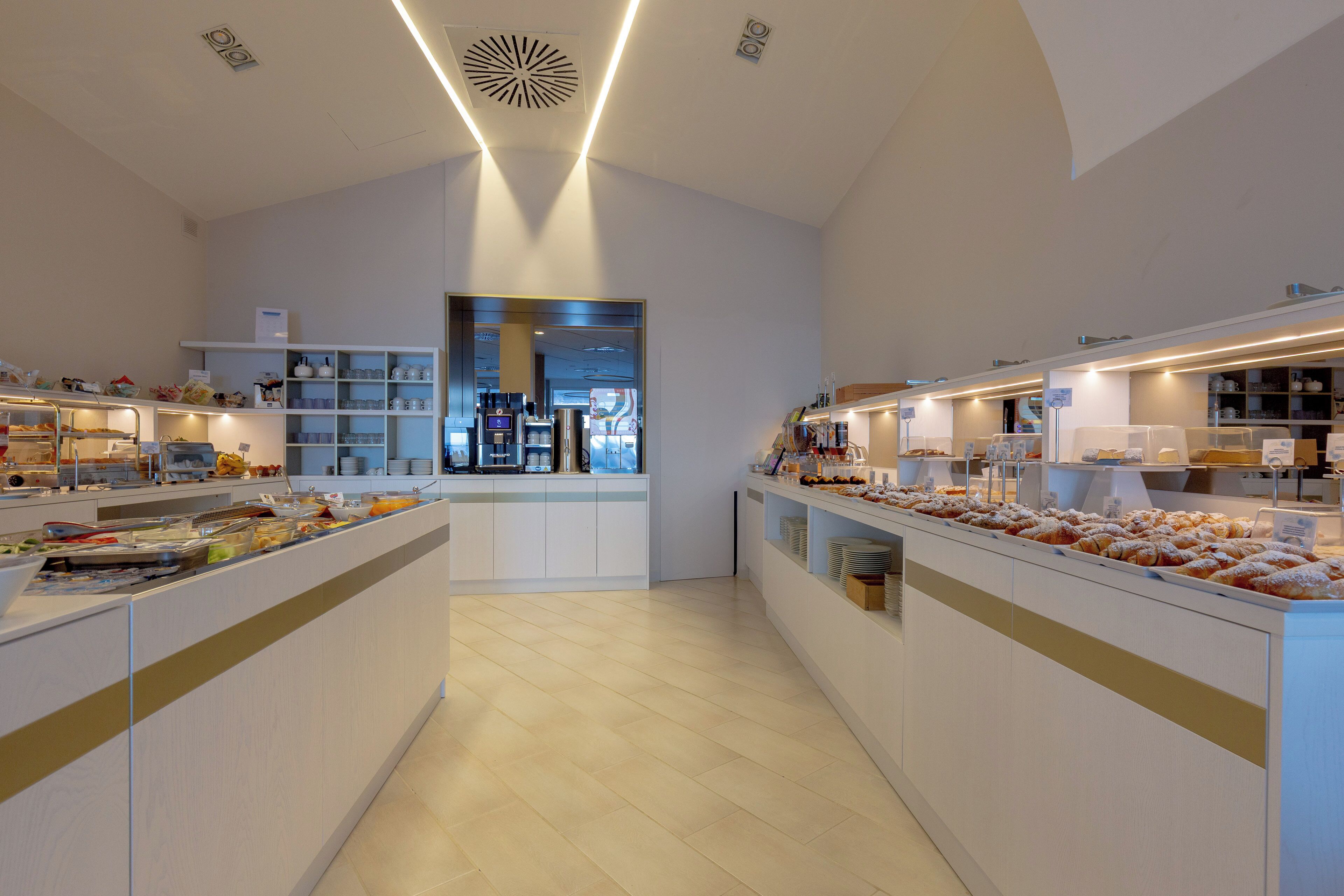 Een moderne hotellobby met een centraal receptiegedeelte, een koffiebar en een buffet met diverse gerechten.