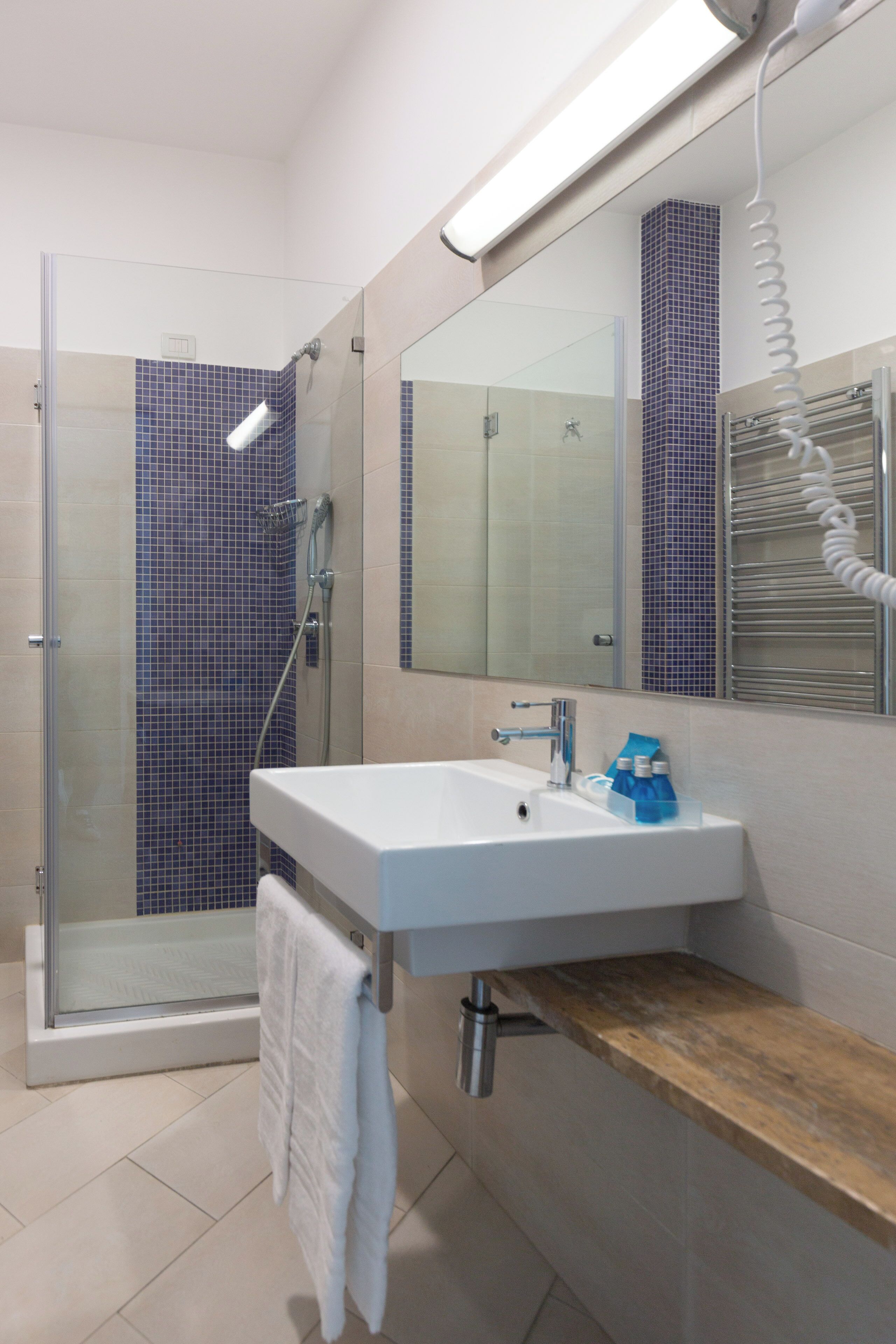 A modern bathroom with a glass shower enclosure, a white sink with a wooden shelf, and a towel hanging on a rack.