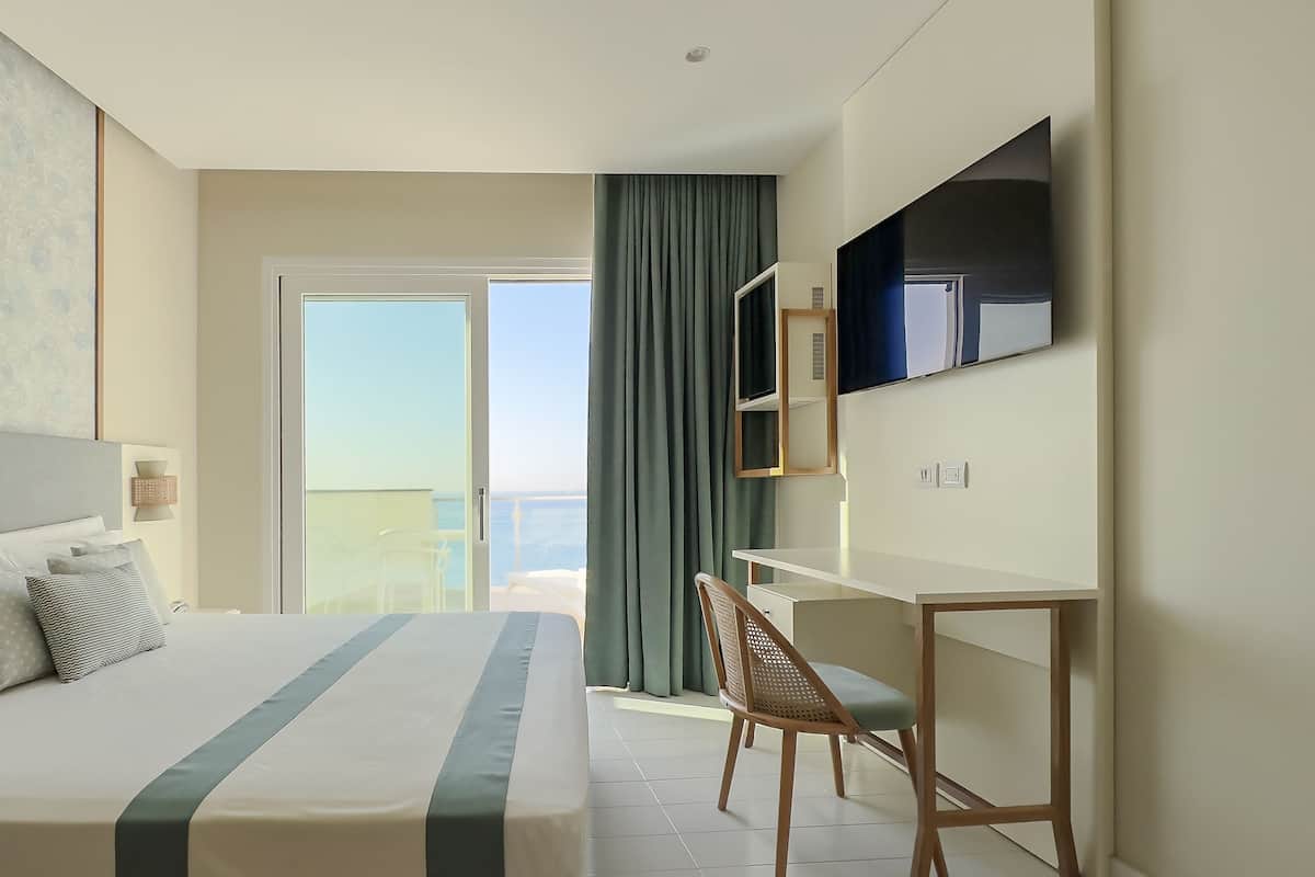 Habitación de hotel con cama, escritorio, silla, televisor y vista al mar.