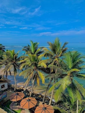 A beach view with palm trees, a restaurant, and the ocean. - Panorama Guesthouse (Beruwala)