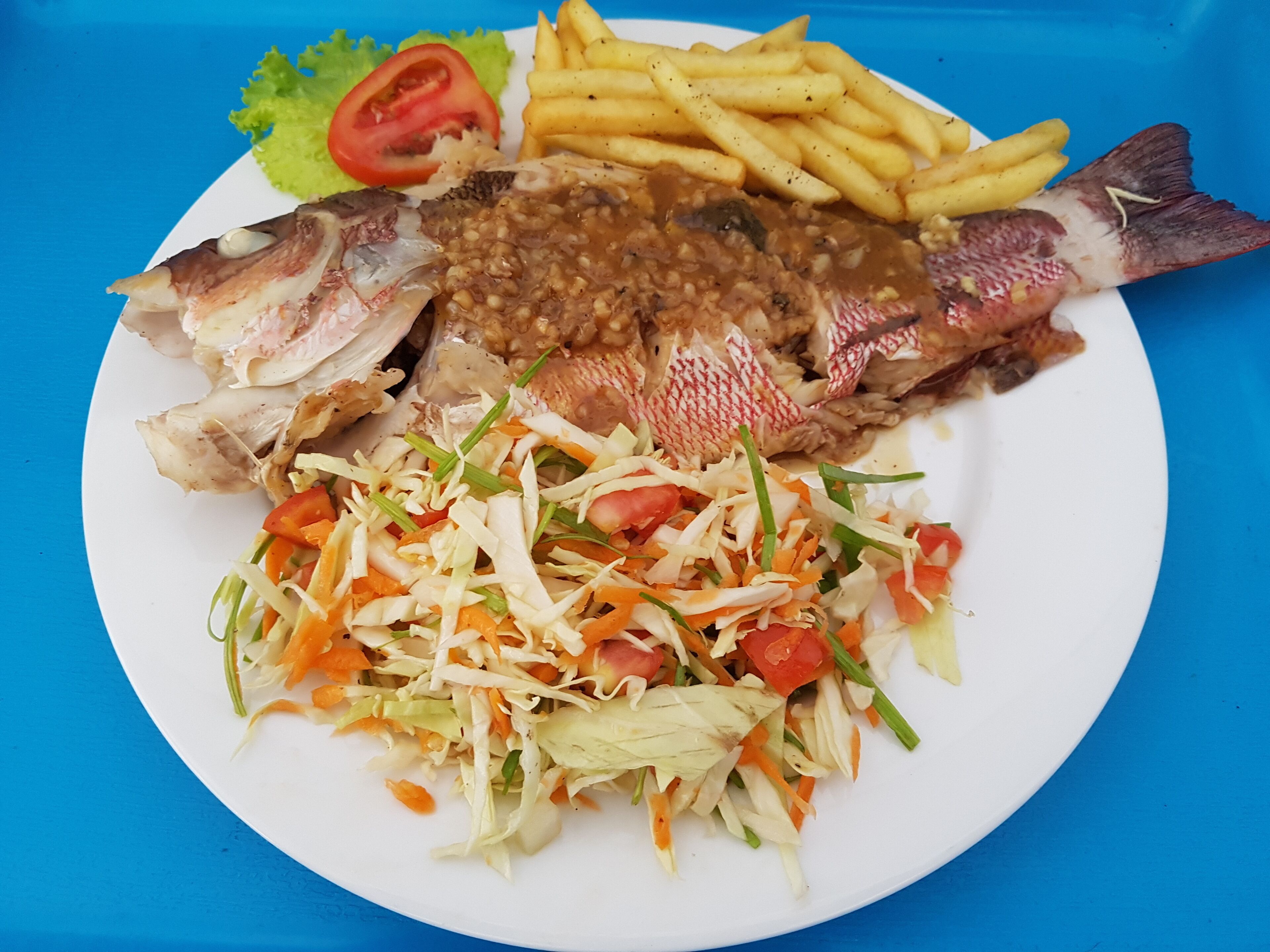 Un plato con pescado, papas fritas, ensalada y una rodaja de tomate.