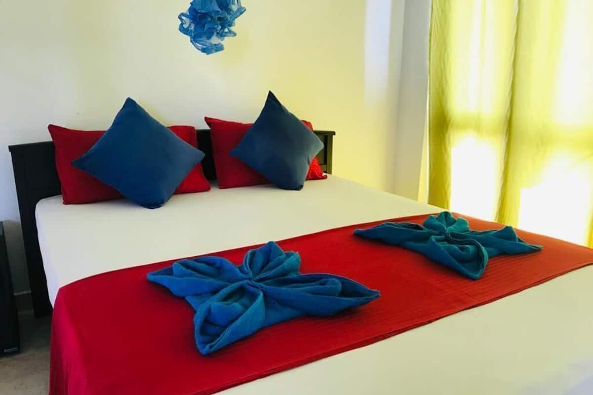 Un lit avec une literie rouge et bleue, des oreillers et un élément décoratif bleu sur le mur.