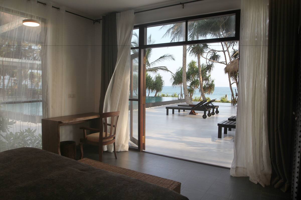 A bedroom with a large window, a desk, and a chair.