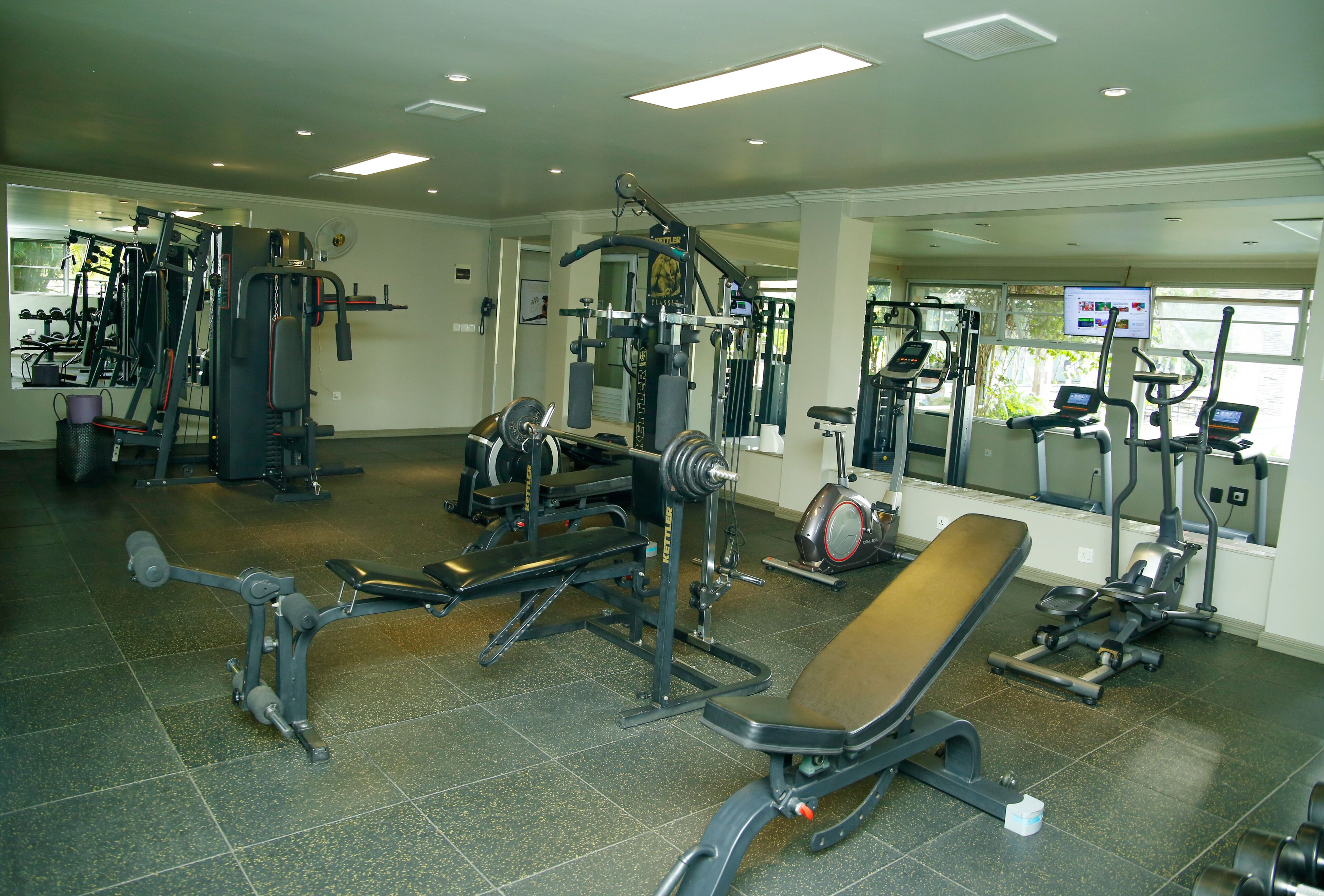 Un gimnasio con diferentes máquinas de ejercicio, una banca y un espejo.