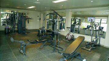 Un gimnasio con diferentes máquinas de ejercicio, una banca y un espejo.