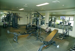 Un gimnasio con diferentes máquinas de ejercicio, una banca y un espejo.