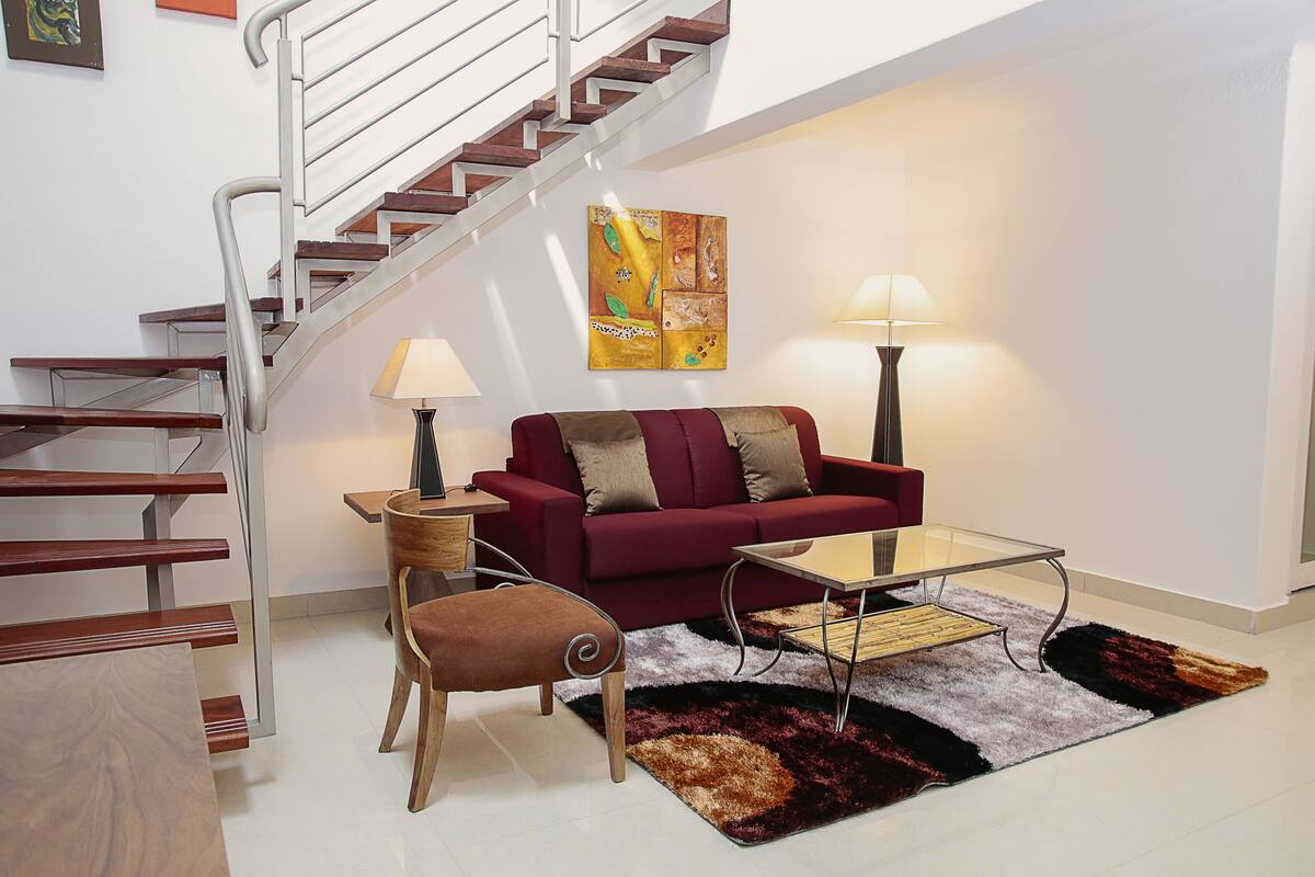 Una sala de estar moderna con una escalera, un sofá rojo, una mesa de centro de vidrio y un tapete estampado.