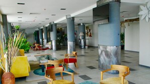 Un hall d’entrée spacieux, doté d’un mobilier moderne, notamment une table en verre avec des magazines, et de grandes colonnes.