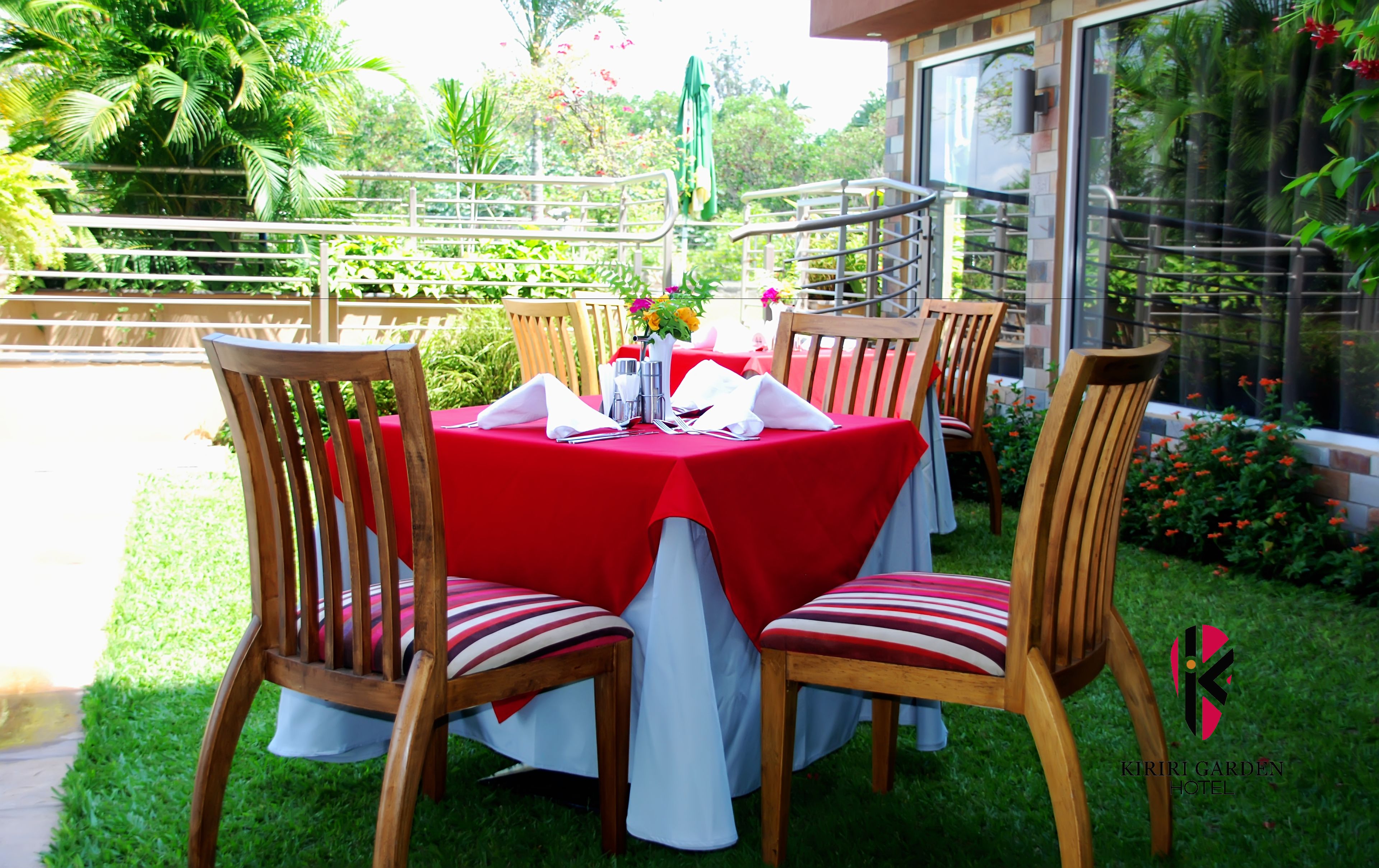 An outdoor dining area with a red tablecloth, wooden chairs, and a glass railing.