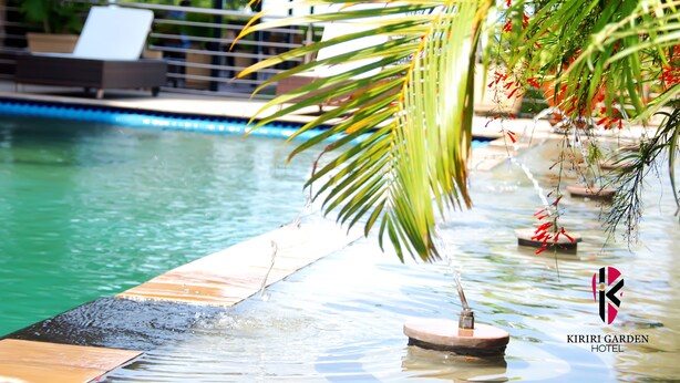 Un espace piscine comprenant des chaises longues, des palmiers et un élément décoratif aquatique.