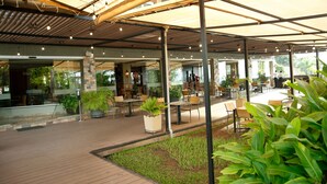 Un espace extérieur aménagé en terrasse, avec un sol en bois, des plantes en pot, ainsi que des tables et des chaises placées sous une tonnelle.