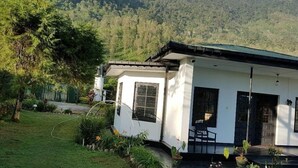 A white building with a green roof, surrounded by a well-maintained garden and a mountainous backdrop. - Royal Eco Resort (Haldummulla)