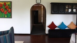 A living room with a sofa, a painting of tulips, a clock, and a cabinet with glass doors. - Royal Eco Resort (Haldummulla)