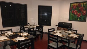 A dining area with a round table and chairs, a grill, and a painting of tulips on the wall. - Royal Eco Resort (Haldummulla)