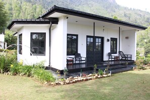 A modern white building with a black roof, a covered porch with chairs, and a stone pathway leading to the entrance. - Royal Eco Resort (Haldummulla)