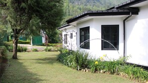 A white building with black-framed windows, surrounded by a well-maintained garden with various plants and a tree. - Royal Eco Resort (Haldummulla)