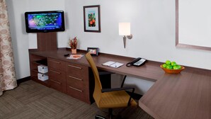 A hotel office with a desk, chair, television, framed picture, lamp, telephone, and a bowl of fruit.