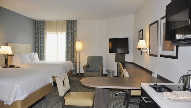 A hotel room with two beds, a dining table, a TV, and a small seating area.