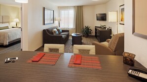 A hotel room with a bed, a sofa, a dining table with placemats, a television, and a plant.