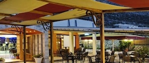 An outdoor dining area with tables and chairs, covered by a canopy, and a view of a mountainous landscape in the background.