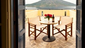 Een balkon met een tafel en stoelen, een vaas met bloemen en een fles. Op de achtergrond is een berg te zien.