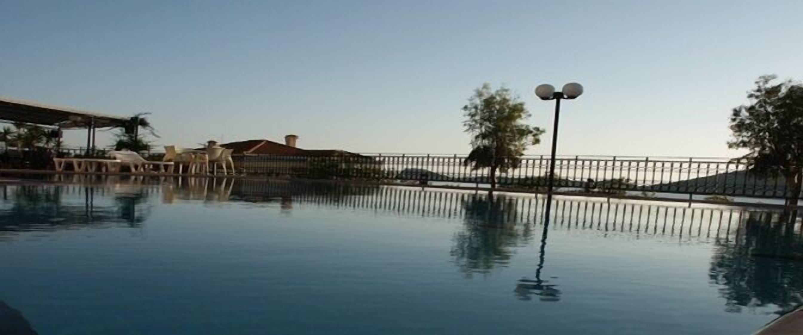 Una piscina tranquila con valla y farola, rodeada de árboles y edificios.
