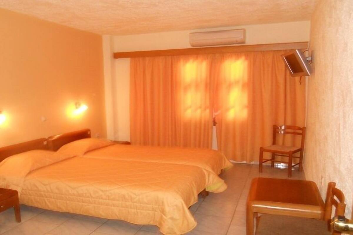 Ein Hotelzimmer mit zwei Betten, einem Sessel, einem Schreibtisch und einem Fernseher.