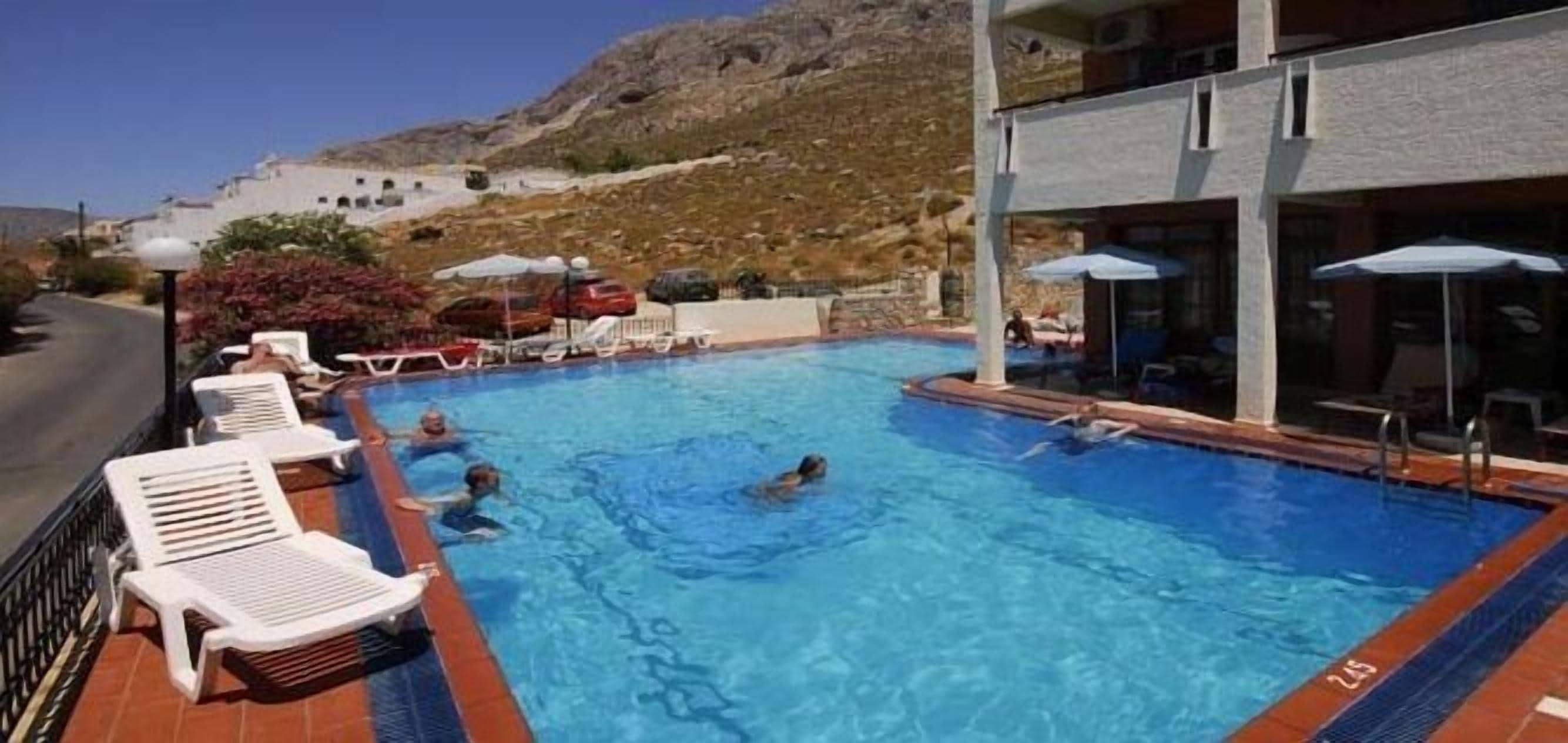 A swimming pool with people swimming and lounging, surrounded by a building with a view of a hillside.