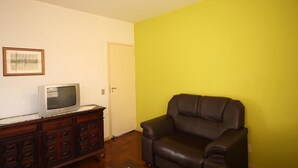 Een kamer met een houten kast, een televisie, een zwarte lederen fauteuil en een deur.