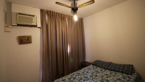 Een slaapkamer met een bed, een plafondventilator, een airconditioning en een gordijn.