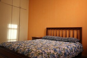 Un dormitorio con colcha estampada, cabecera de madera, mesita de noche y armario.