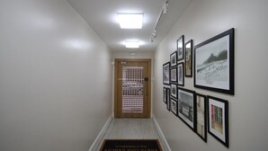 Een gang met een houten deur, ingelijste foto's aan de muur en een deurmat met tekst.