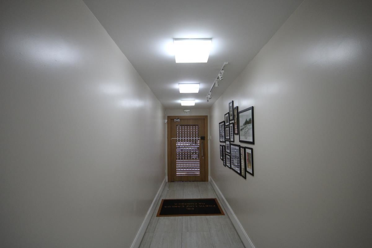 A hallway with a wooden door, framed pictures on the wall, and a doormat at the entrance.