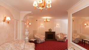 Una habitación con alfombra roja, dos sillones, un sofá, una chimenea y un espejo grande.