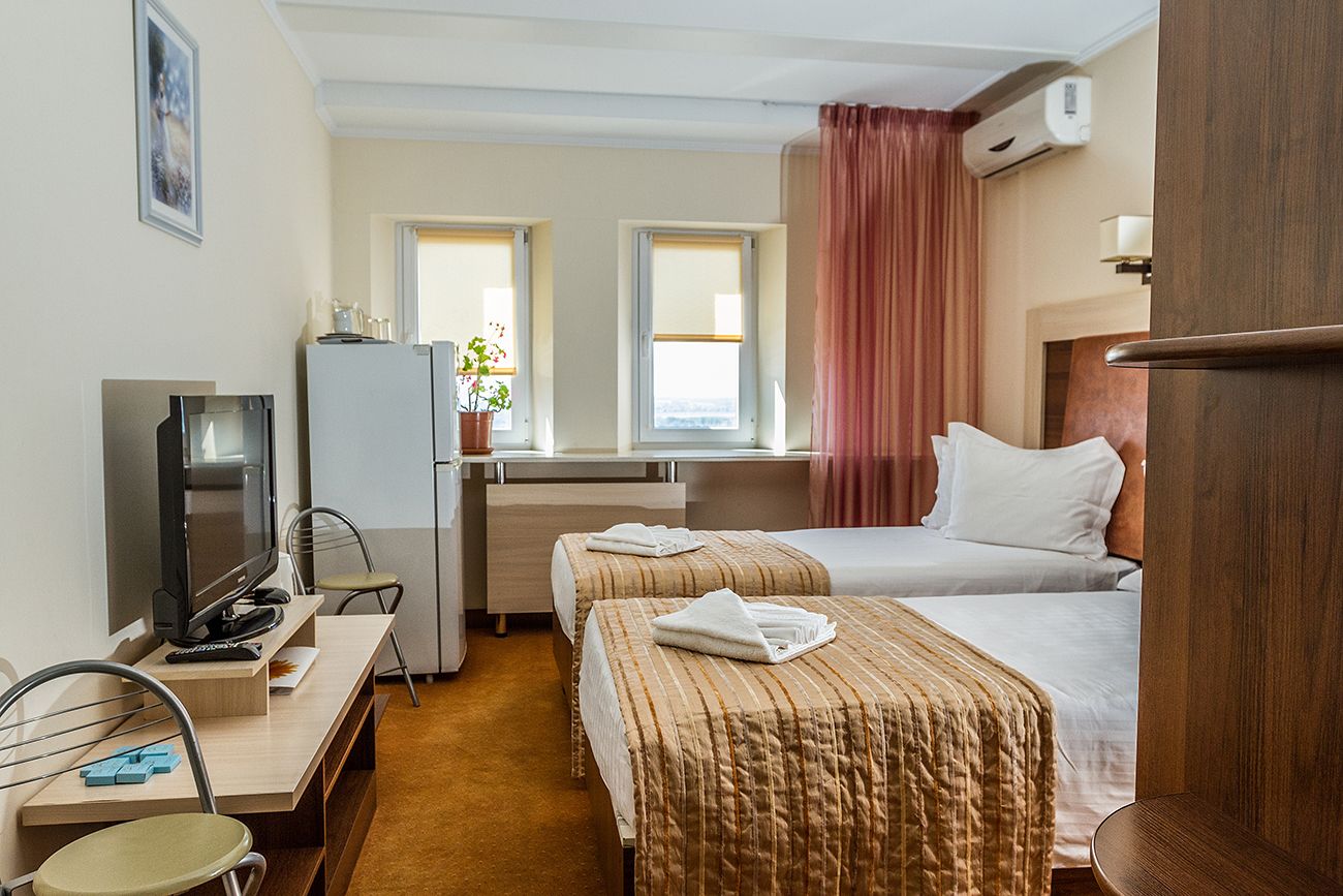 Ein Hotelzimmer mit zwei Betten, einem Schreibtisch, einem Fernseher, einem Kühlschrank und einem Fenster mit Vorhängen.