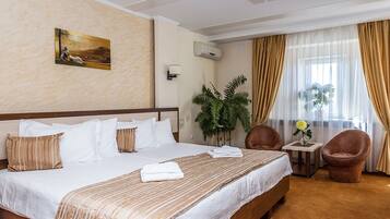Habitació d'hotel amb un llit gran, una taula petita amb un ram, dues cadires i un quadre a la paret.