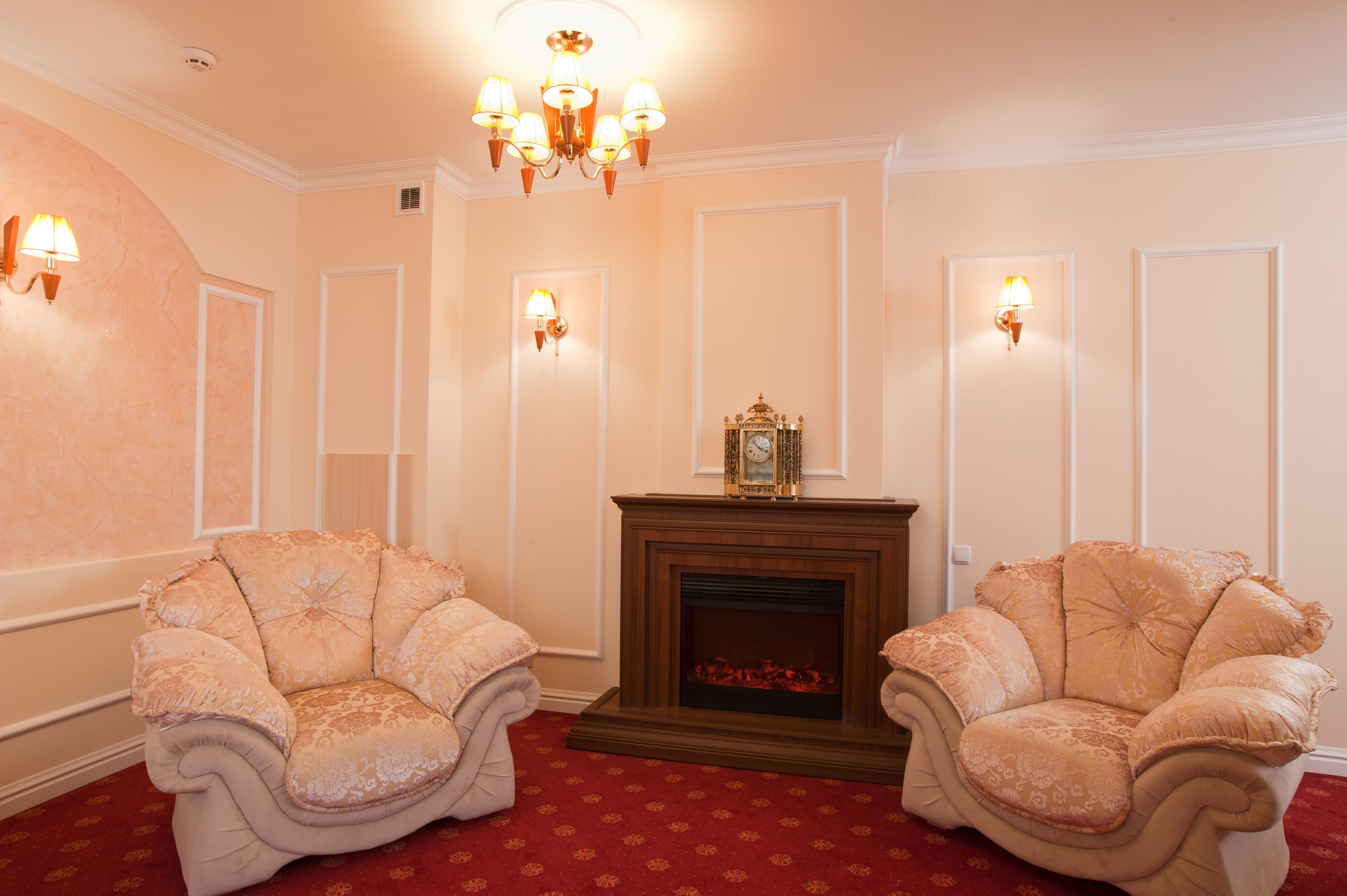 A room with two ornate armchairs, a fireplace, and wall sconces.